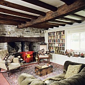 Wohnraum mit rustikaler Holzbalkendecke und Natursteinwand mit rotem Kaminofen in Kaminnische