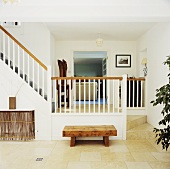 Moderne weiße Eingangshalle mit Treppe und rustikaler Holzbank auf Fliesenboden