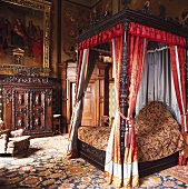 Himmelbett aus geschnitztem Holz und roten Vorhängen mit Orientteppich im Schlafzimmer eines eleganten Landhauses