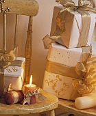 Weihnachtsgeschenke mit weißem Papier und goldenem Band auf rustikalem Stuhl mit Kerzenlicht