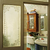 Geätzte Glasscheibe neben offener Badtür und Blick auf schlichte Badeinrichtung