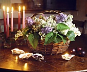 Weisser und violetter Flieder im Korb neben brennenden Kerzen