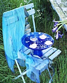 Schwimmende Kerzen in blauer Glasschale auf pastellblauem Stuhl