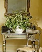 Weißes Blumenarrangement in weißer Schale auf ländlichem Wandtisch mit passendem Stuhl