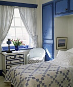 Einbauschrank mit blauen Fronten und Kommode vor Schlafzimmerfenster im ländlichen Stil