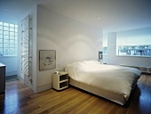 A white, open-plan bedroom with a double bed and parquet flooring