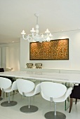 A white table with white designer chairs, a white chandelier and a colourful picture on a white wall in an elegant conference room