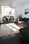 A large paper lampshade hanging above a beige flokati rug in a living room with black seats