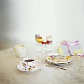 A cup of coffee, cake plate and petit fours on a table