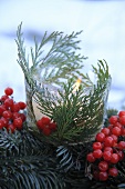 A burning red candle in an ice cream dish decorated wit thuja