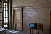 Wohnraum mit altem Fernseher auf Tischchen vor brauner Wand mit Holztür