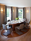 Classic dining room with cantilevered chairs upholstered in gray around an oval table and gray floor length curtains at the window