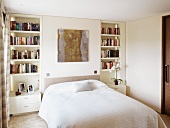 White bedroom with a double bed and built-in shelves with nightstands