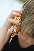Child holding a sea shell to its ear
