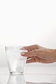 A hand holding a glass with an effervescent tablet