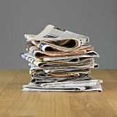 A stack of newspapers on a wooden surface in front of a grey wall