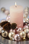 A pink candle with Christmas baubles and pine cones