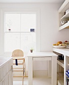 weiße, helle Küche mit Kinderhochstuhl und schlichtem Tisch am Fenster