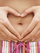 A woman's hands in a heart shape around her navel