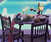 Cheese board, olives, white bread & red wine on table by pool