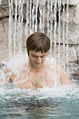 Young man standing under a waterfall