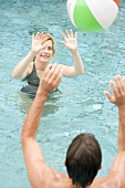 Man and woman playing with beach ball in swimming pool