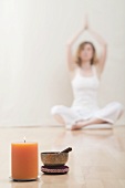 Young woman meditating, candle and singing bowl