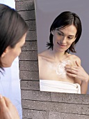 Woman in front of mirror putting cream on her chest
