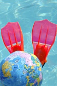 Flippers and globe beach ball in swimming pool