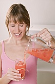 Frau giesst rosa Grapefruitsaft in Glas