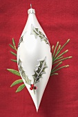 White tear-drop shaped Christmas bauble on red linen cloth