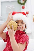 Small girl in Father Christmas hat holding Christmas bauble
