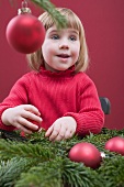 Kleines Mädchen schmückt Christbaum mit roten Kugeln