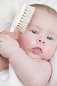 Hand brushing a baby's hair with a soft brush