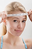 Woman holding tape measure against her forehead