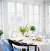 Gedeckter Esstisch mit Blumenstrauss am Fenster einer verglasten Veranda