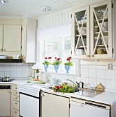 Einbauküche mit hellen Holzmöbeln, einem Sprossenfenster und Geranientöpfen auf dem Fensterbrett