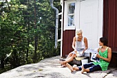 Zwei Frauen waschen Geschirr vor einem Holzhaus (Schweden)