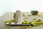 Buddhakopf auf Tablett, verstreute Blätter