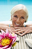 Germany, Senior woman leaning on edge of pool, portrait