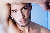 Young man under shower behind glass pane, close-up