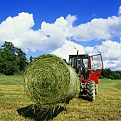 Tractor with a round bale of hay in a field