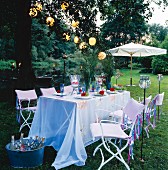 A festively laid table in a garden decorated with flowers, lanterns, lantern garlands and torches