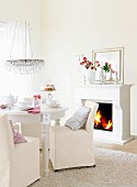 An elegant living room in white with a table laid in front of an open fire