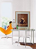 Plexiglas Stuhl vor Schreibtisch mit Foto von Sumoringer im Holzrahmen, im Hintergrund gelber Designersessel