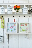 Weisses Küchenbord mit alten Aufbewahrungsdosen und Papier-Schmetterlinge in Bildrrahmen an weisser Holzwand