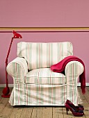 Armchair with striped cover and red metal standard lamp against pink wall
