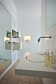 A modern, white bathroom with a wash basin, a wall mirror and drawers set into the wall