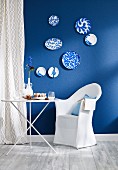 Small dining area with folding table and chair with loose cover against wall with blue wallpaper and blue and white decorative wall plates