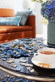 Jigsaw pieces and cup of tea on coffee table with leather couch in background